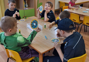 5 chłopców przy stoliku ozdabia papierowe pączki kolorowymi trójkącikami.